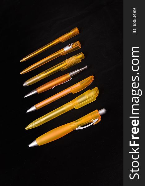 Seven orange plastic pens on black ground