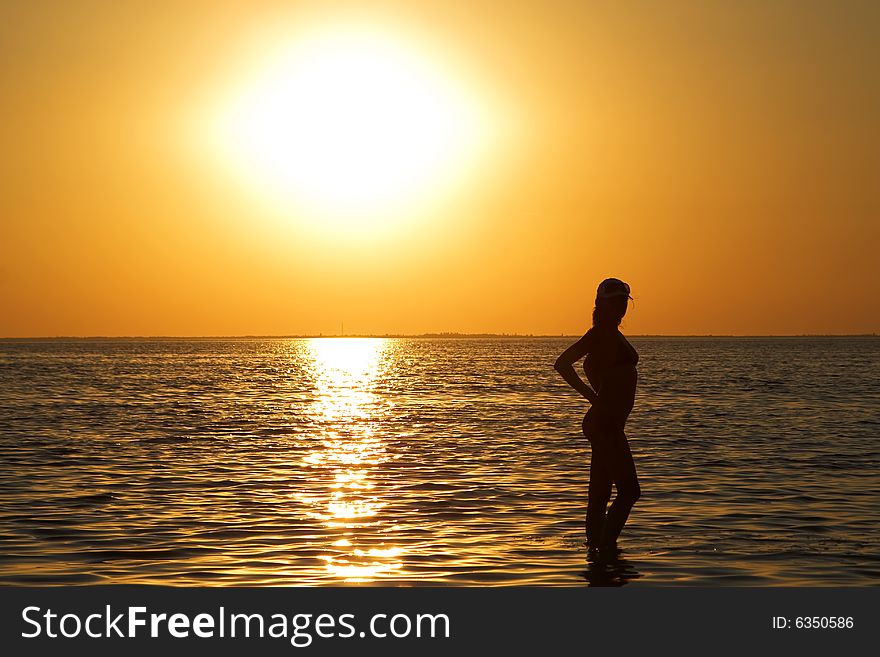 Silhouette of the young woman on a sea bay on a sunset
