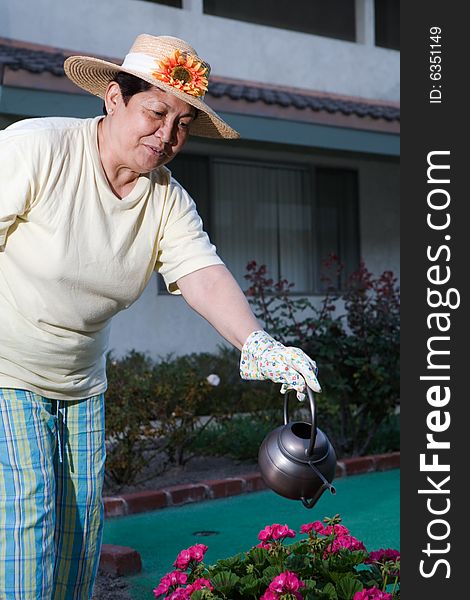 Senior Asian woman wearing straw hat outdoors watering flowers. Senior Asian woman wearing straw hat outdoors watering flowers