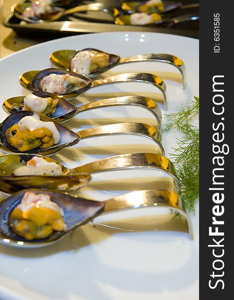 A freshly prepared delicious black mussel starter, beautifully presented on silver spoons in a curved white plate.