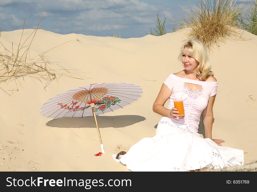 A young woman sits on sand with glass of juice and umbrella. A young woman sits on sand with glass of juice and umbrella