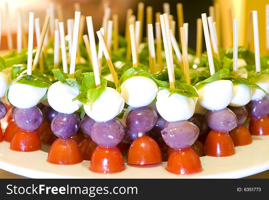 Snacks prepared to be served at a function, consisting of Bocconccini cheese, olive, tomato and a basil leaf on a skewer. Snacks prepared to be served at a function, consisting of Bocconccini cheese, olive, tomato and a basil leaf on a skewer.