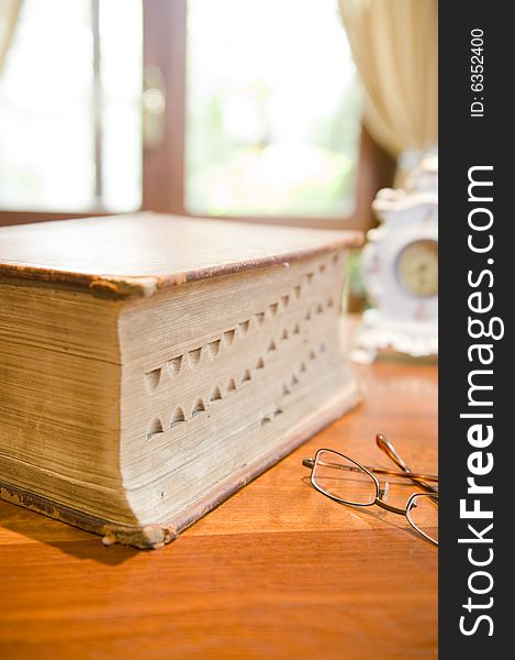 An antique reference book with eyeglasses and an old clock.