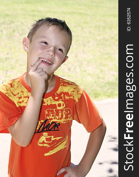 A little boy in an orange sport shirt shows a finger on the healthy teeth