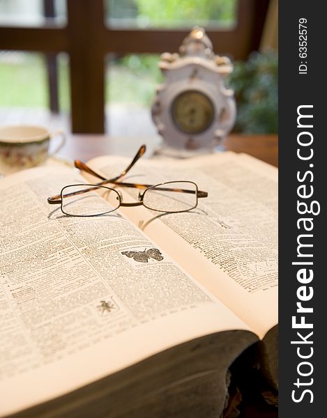 An antique reference book with eyeglasses and an old clock.