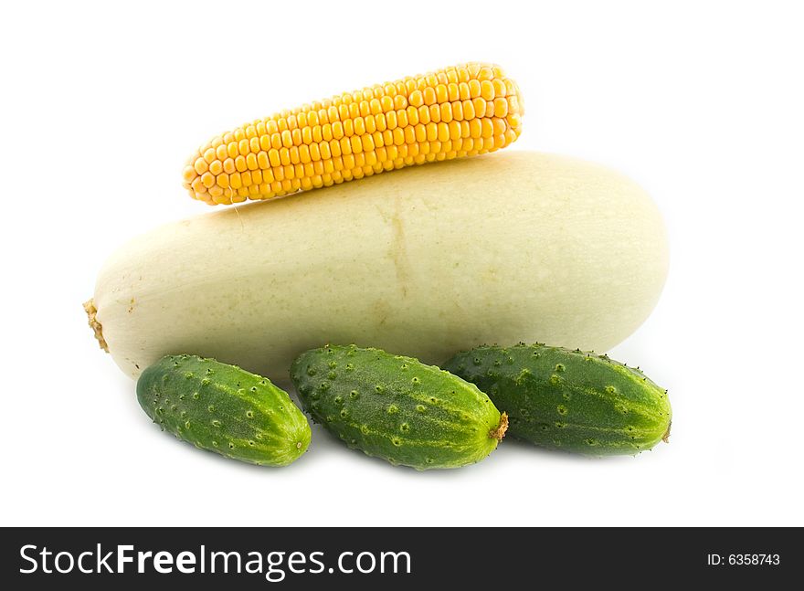 Corn on a vegetable marrow and green cucumbers on a white background