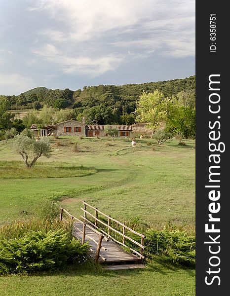 View of a luxury country house in the famous tuscan hills, Italy. In foreground the small wooden bridge of the villa's garden. View of a luxury country house in the famous tuscan hills, Italy. In foreground the small wooden bridge of the villa's garden.