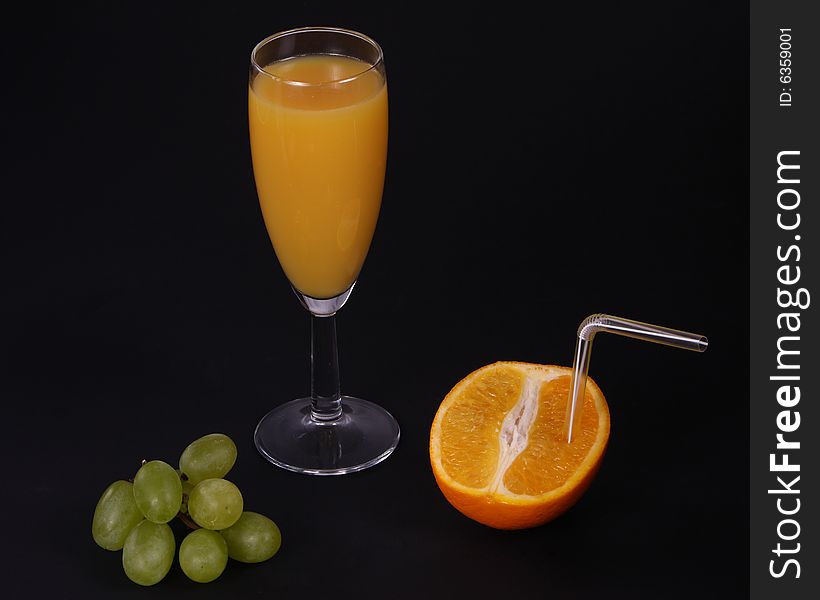 A freshly squeezed orange drink with half orange and grapes. A freshly squeezed orange drink with half orange and grapes