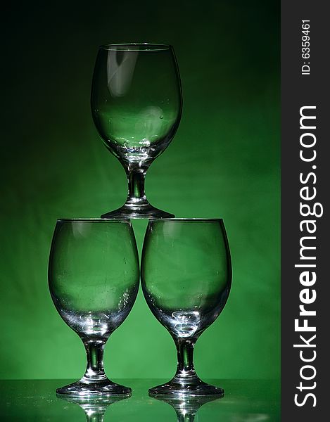 Three wine glasses forming a pyramid, on dark green unregular background, lit from below. Three wine glasses forming a pyramid, on dark green unregular background, lit from below