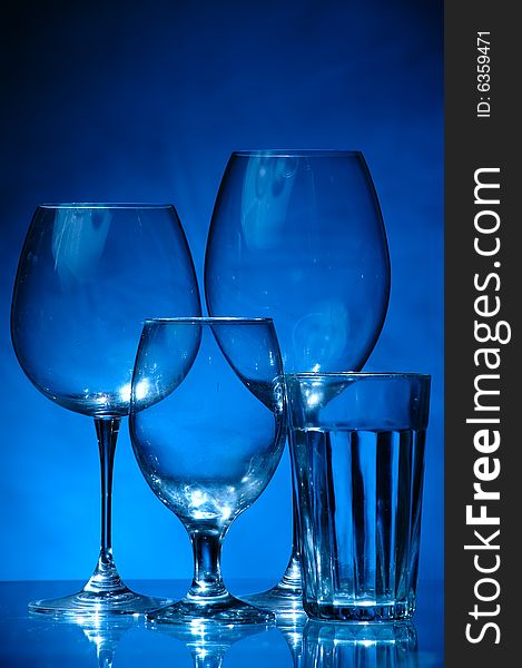 Four different glasses standing next to each other on blue background, like a family. They all different but they all glasses. Four different glasses standing next to each other on blue background, like a family. They all different but they all glasses.