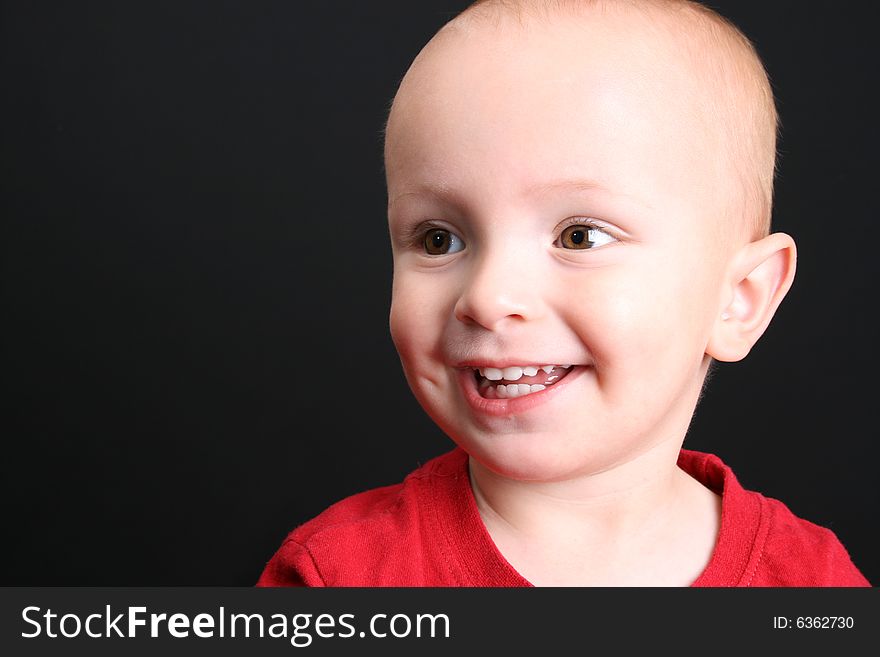 Blonde toddler against a black background with a big smile