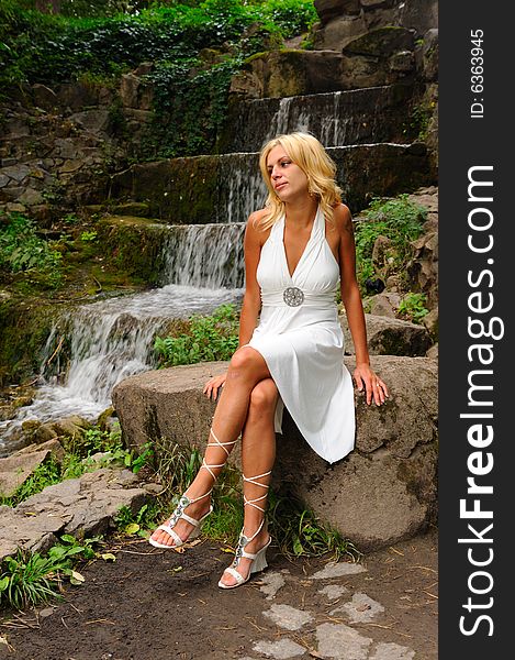 Woman in white dress sitting near waterfall