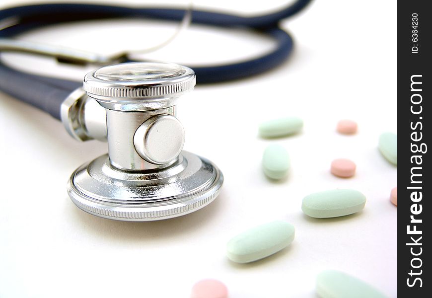 Silver metal stethoscope with pills over white background