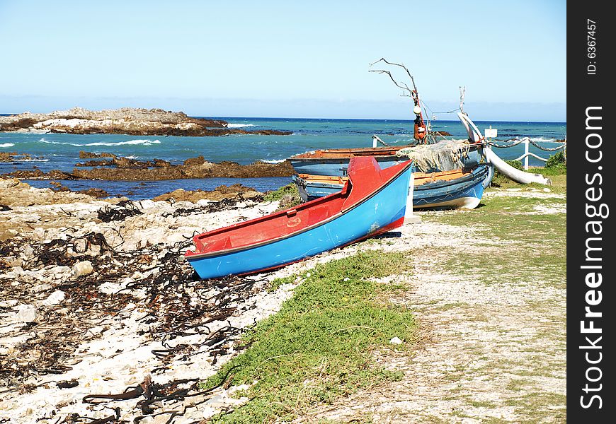 2 old fishing boats on land with a shore covered in bamboo and rocks and the sea in tha background