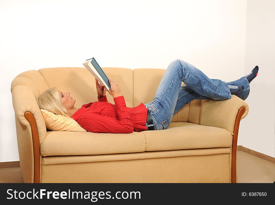 Young woman at home, lying on a sofa. Reading a book.