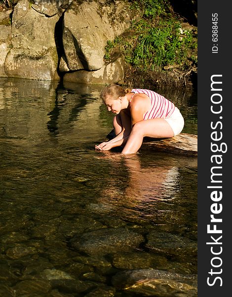 Young woman drinking water in the mountain river