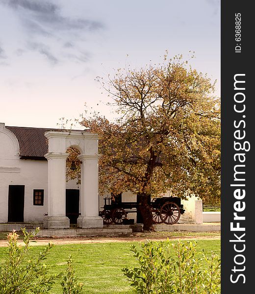 An old slave bell with an oak tree and wagon infront of a Thatched Cape Dutch Hoestead. An old slave bell with an oak tree and wagon infront of a Thatched Cape Dutch Hoestead