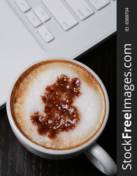 A cup of cappucino with dollar sign on computer's keyboard