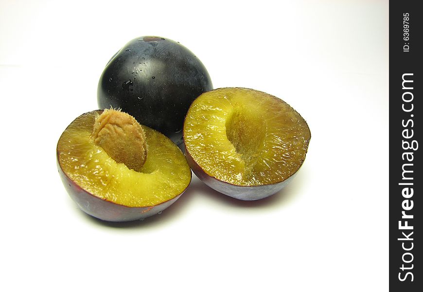 A single plum behind another plum that was cut in half on a white background. A single plum behind another plum that was cut in half on a white background.