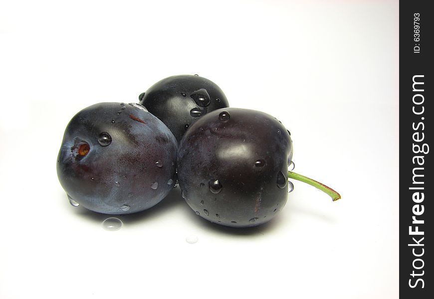 Three plums that were sprayed with water on a white background.