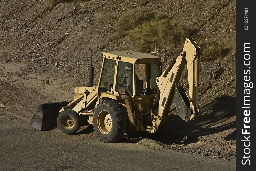 This is a picture of a tractor with a backhoe loader and a scoop at work on a roadway. This is a picture of a tractor with a backhoe loader and a scoop at work on a roadway.