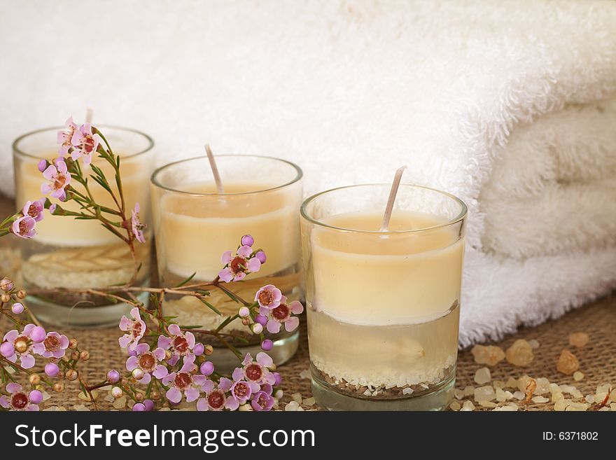 Relaxing spa scene with a white rolled up towel, pink flowers, beautiful handmade candles and bath salts