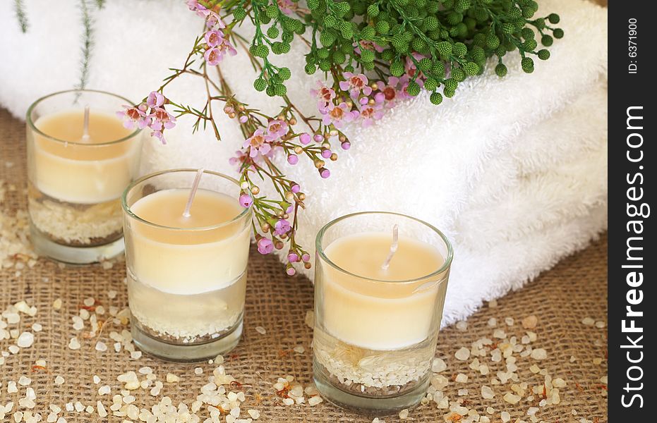 Relaxing spa scene with a white rolled up towel, pink and green flowers, beautiful handmade candles and bath salts