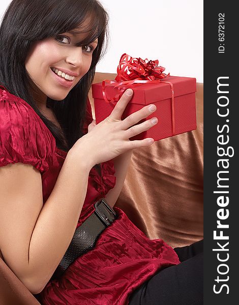 Portrait of a beautiful young brunette woman sitting on a couch and holding a gift box at a celebration. Not isolated. Portrait of a beautiful young brunette woman sitting on a couch and holding a gift box at a celebration. Not isolated