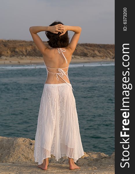 Young woman wearing white dress during sunset at beach staying on the rock