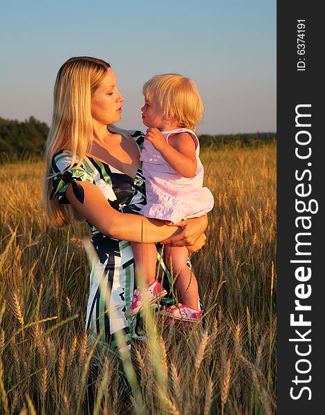 Mother holds child on hands in a wheaten field