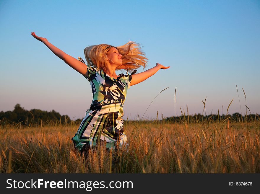 Girl with lifted hands and flying hair on a wheaten field