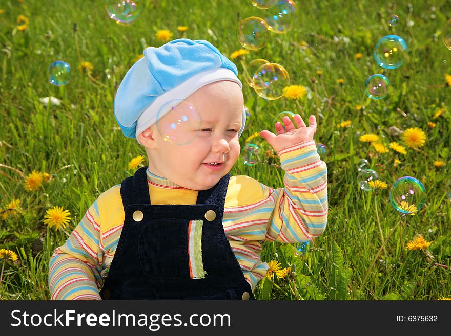 Child sits on grass and looks on soap bubbles