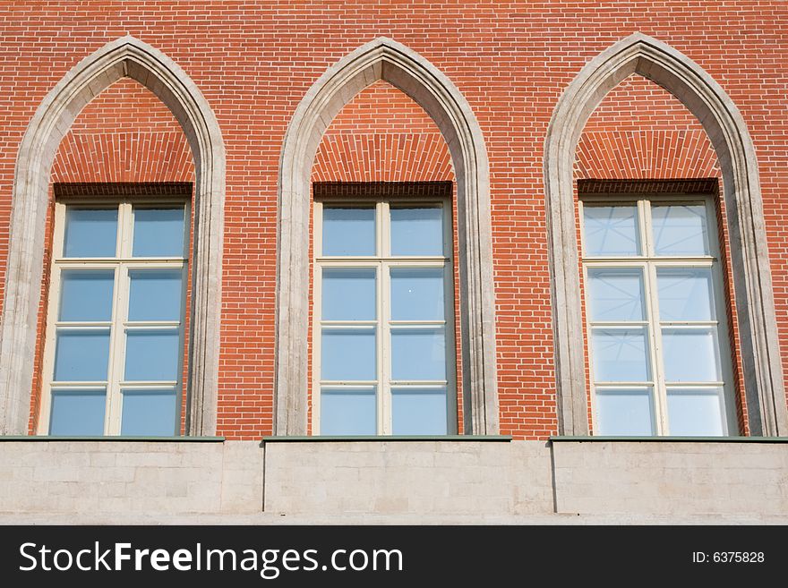 Three high glassed white-framed windows in a red brick wall