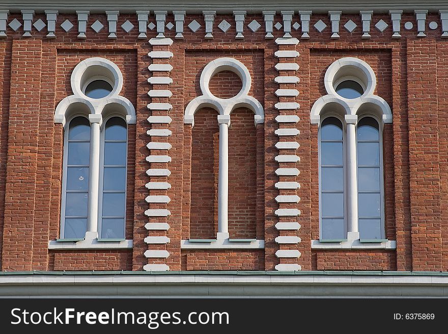 Three high glassed white-framed windows in a red brick wall