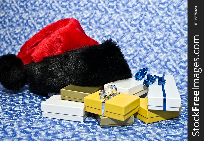 Santa hat with box gifts on a blue winter background. Santa hat with box gifts on a blue winter background.