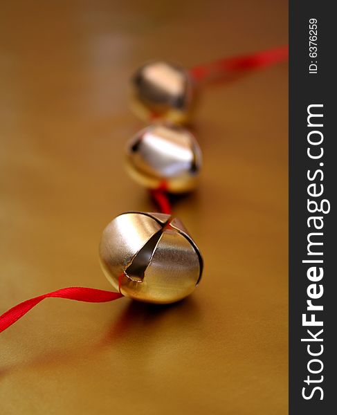 Three gold bells with red ribbon, all on a metallic gold background.