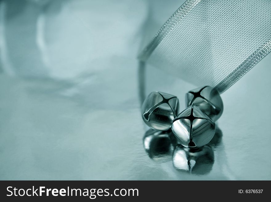 Three bells and silver ribbon reflecting onto a silver metallic background. Shallow depth of filed and selective focus used. Copyspace available. Three bells and silver ribbon reflecting onto a silver metallic background. Shallow depth of filed and selective focus used. Copyspace available.