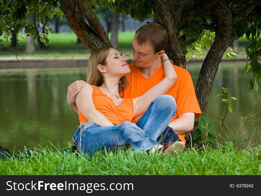 Loving couple kisses under a tree on a river bank