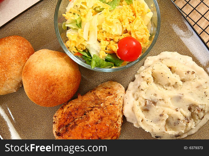 Grilled chicken, mashed potatoes, rolls and salad in plate.