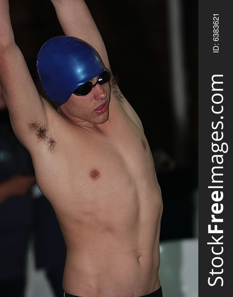 Swimmer preparing for race by stretching out his arms with blue cap