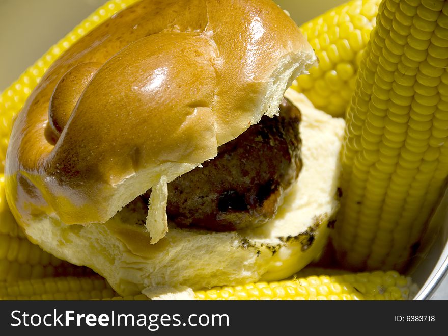Single hamburger on a greasy bun with corn on the side. Single hamburger on a greasy bun with corn on the side