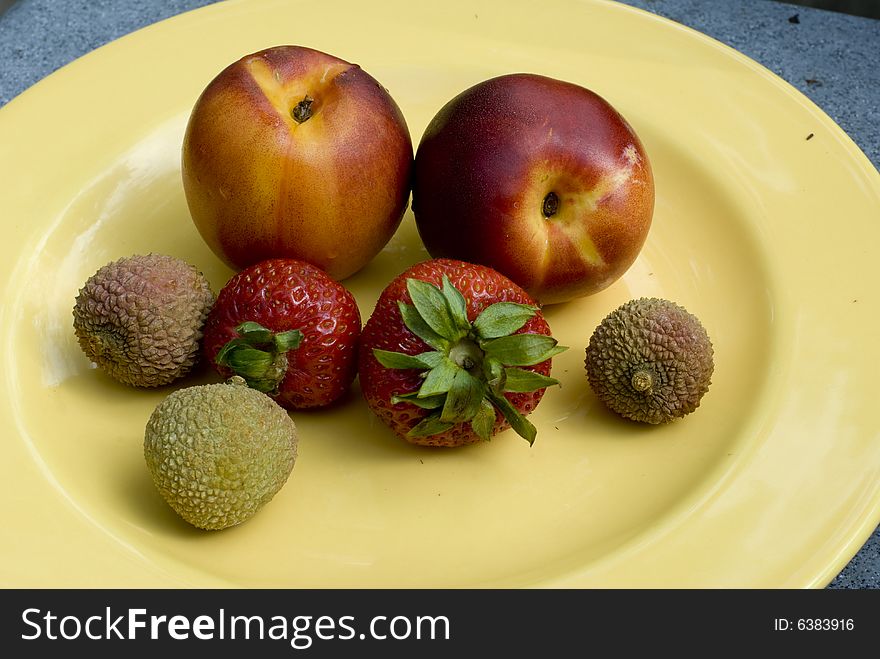 Pair of nectarines, strawberries and lychees on a yellow plate. Pair of nectarines, strawberries and lychees on a yellow plate