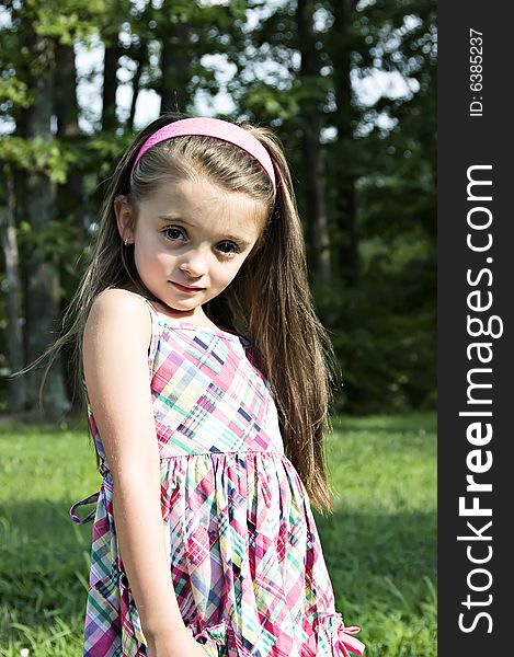 Beautiful Child modeling a plaid sundress in an outdoor setting wearing a pink headband.