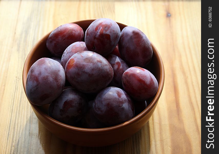 Plums on plate on wooden background