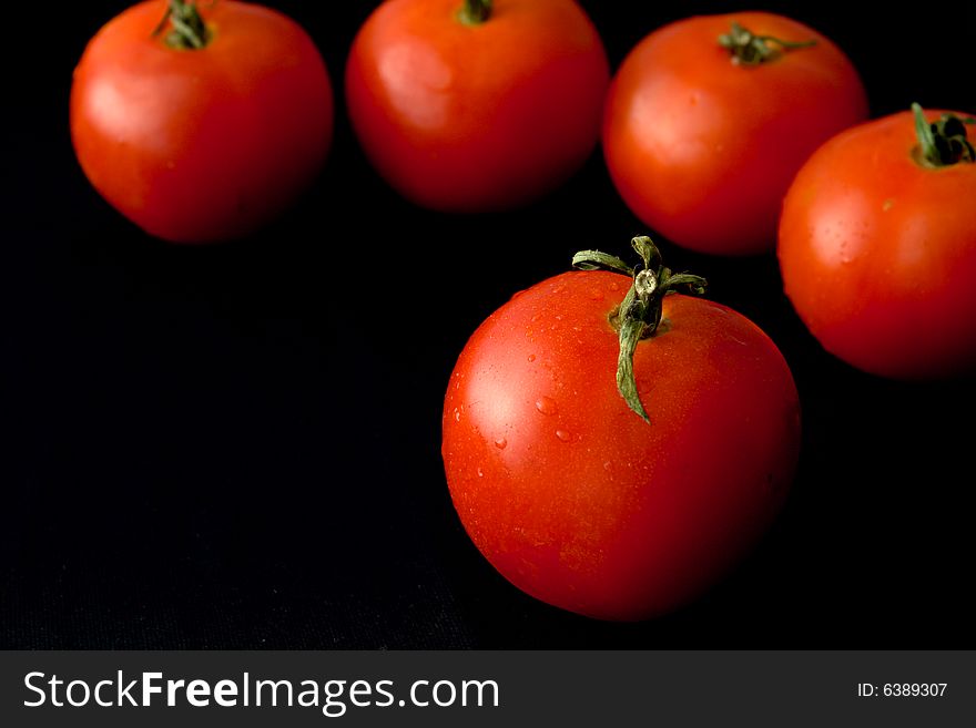 Tomatoes on a black background with drops of water. Even the tomato can look is refined