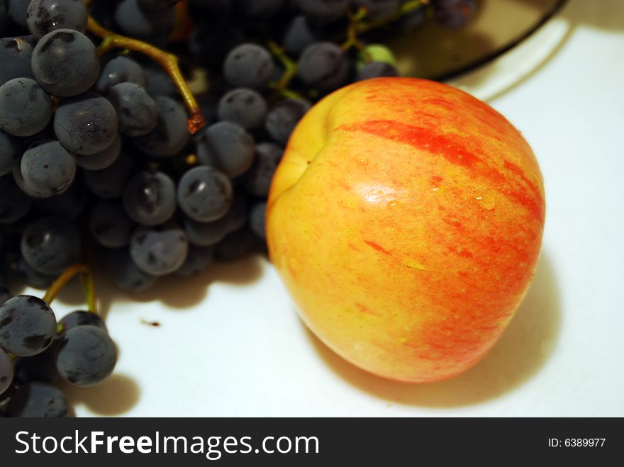 An apple with a drop of water and black grapes details. An apple with a drop of water and black grapes details.