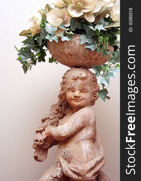 A cherub statue holds flowers on top of its head. A cherub statue holds flowers on top of its head.