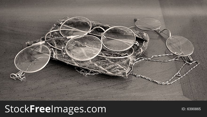 Three pair of antique glasses sit on a wooden table in black and white.