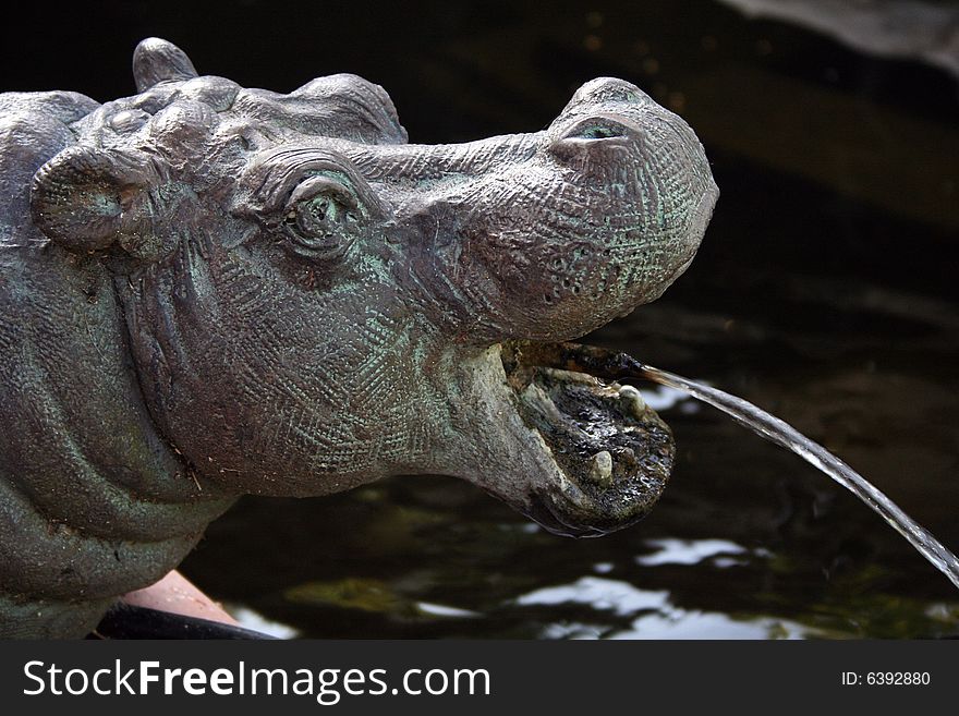 A hippo statue spits water out of its mouth into a pool.