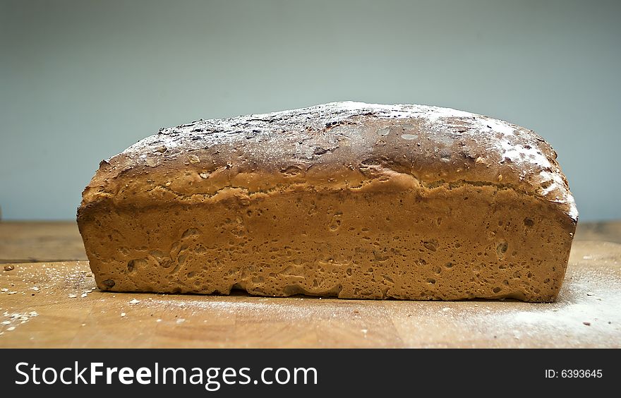 Loaf of whole grain malted bread cooked fresh in an english country kitchen, dusted with flour on a wooden board. Loaf of whole grain malted bread cooked fresh in an english country kitchen, dusted with flour on a wooden board